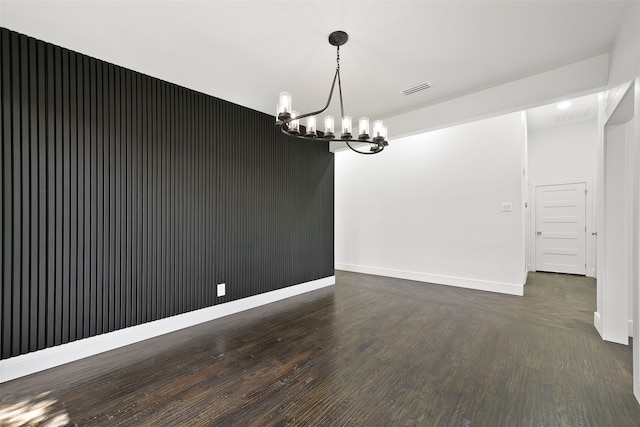 empty room with dark hardwood / wood-style flooring and an inviting chandelier