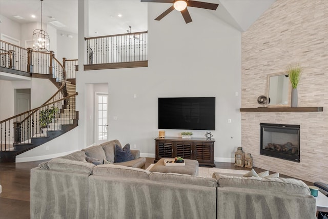 living room featuring ceiling fan with notable chandelier, a fireplace, hardwood / wood-style floors, and a high ceiling