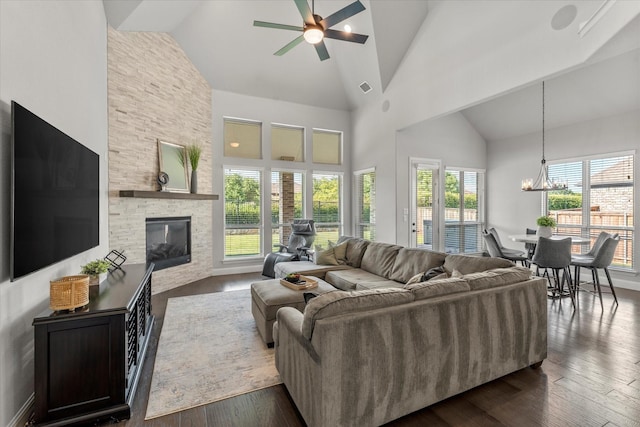 living room featuring dark hardwood / wood-style flooring, ceiling fan with notable chandelier, a fireplace, and high vaulted ceiling