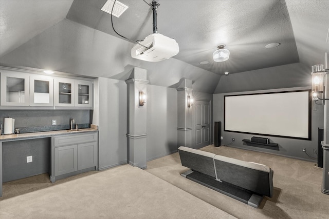 carpeted home theater room with decorative columns, vaulted ceiling, indoor wet bar, and a textured ceiling