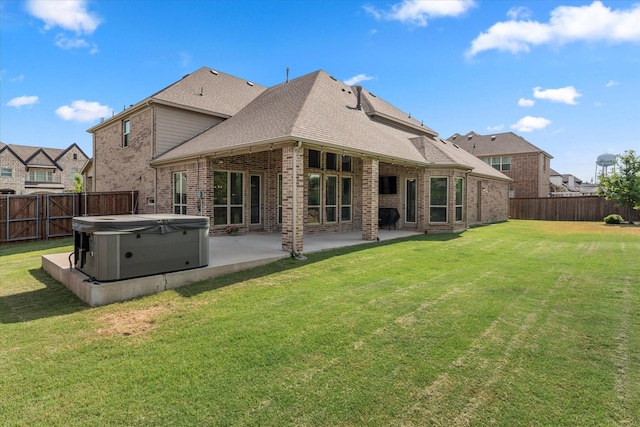 rear view of house featuring a hot tub, a lawn, and a patio area