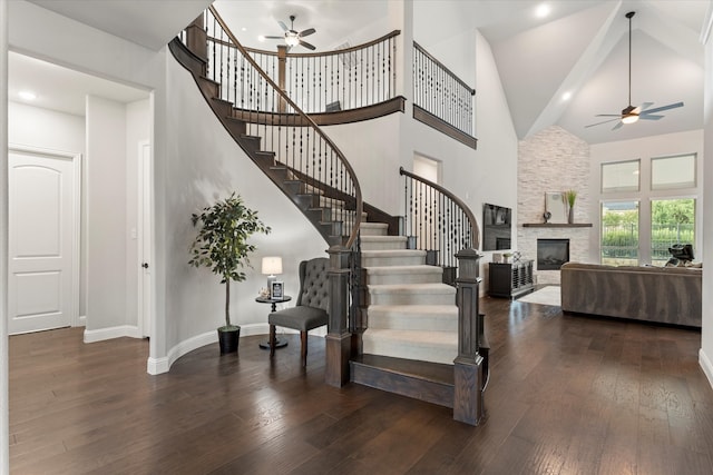 stairway with ceiling fan, high vaulted ceiling, a stone fireplace, and hardwood / wood-style floors