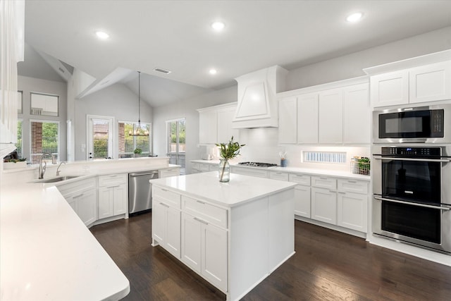 kitchen featuring premium range hood, sink, hanging light fixtures, appliances with stainless steel finishes, and white cabinets