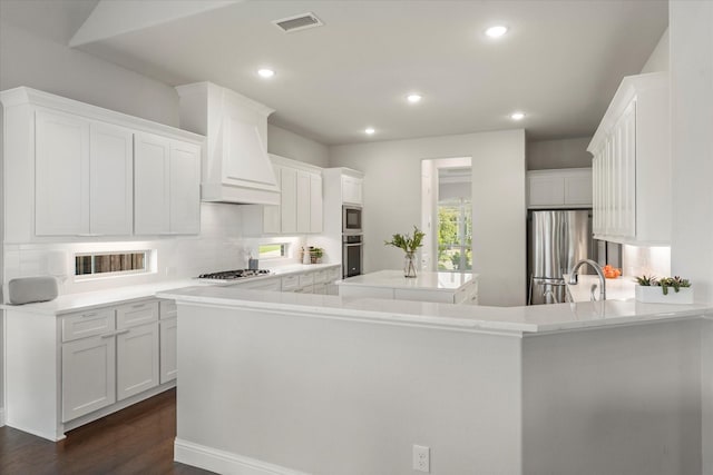 kitchen with appliances with stainless steel finishes, backsplash, white cabinets, a kitchen island, and kitchen peninsula