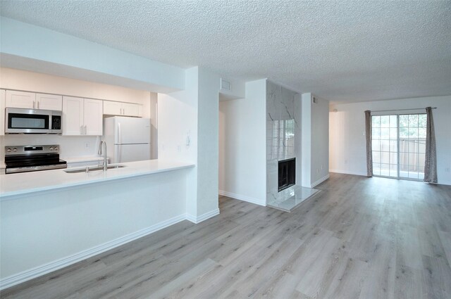 kitchen featuring white cabinets, stainless steel appliances, light hardwood / wood-style floors, a tiled fireplace, and sink