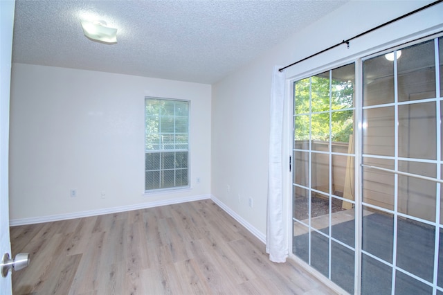 empty room with light wood-type flooring and a textured ceiling