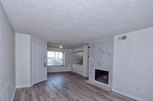 unfurnished living room featuring a high end fireplace, a textured ceiling, and hardwood / wood-style floors