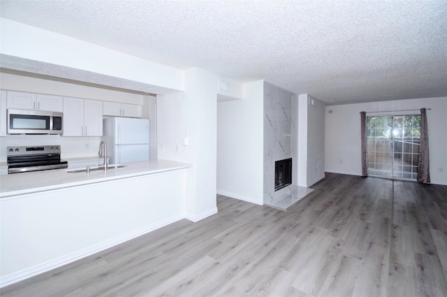 unfurnished living room featuring a premium fireplace, sink, a textured ceiling, and light hardwood / wood-style floors