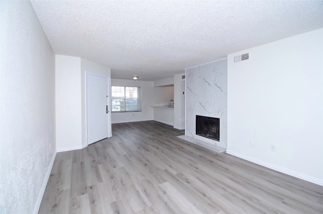 unfurnished living room with light hardwood / wood-style flooring, a high end fireplace, and a textured ceiling