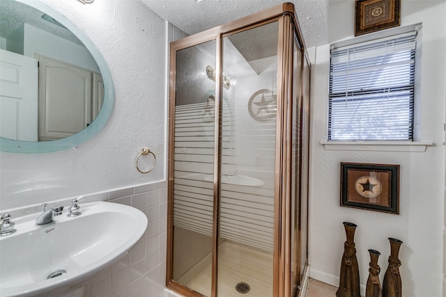 bathroom with tile walls, a textured ceiling, a shower with shower door, and sink