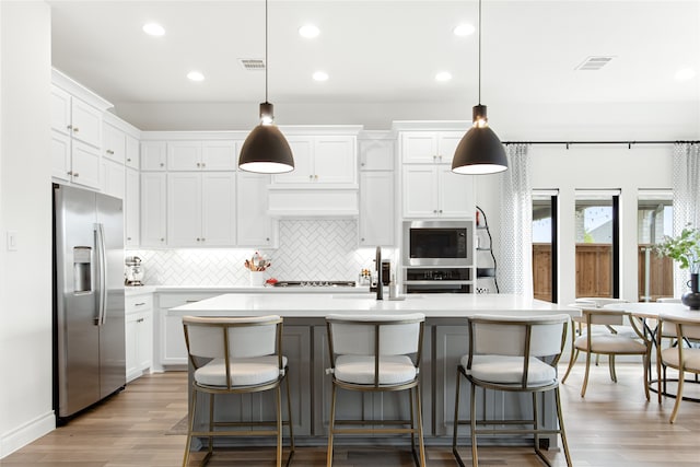 kitchen featuring hanging light fixtures, light hardwood / wood-style floors, decorative backsplash, a kitchen island with sink, and stainless steel fridge with ice dispenser