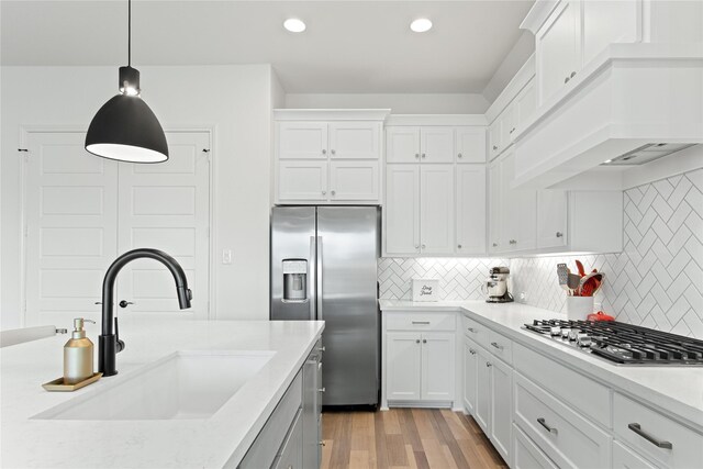 kitchen featuring white cabinetry, custom range hood, light wood-type flooring, backsplash, and stainless steel appliances