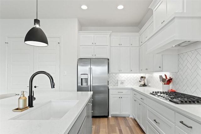 kitchen featuring premium range hood, appliances with stainless steel finishes, light wood-style floors, white cabinets, and a sink