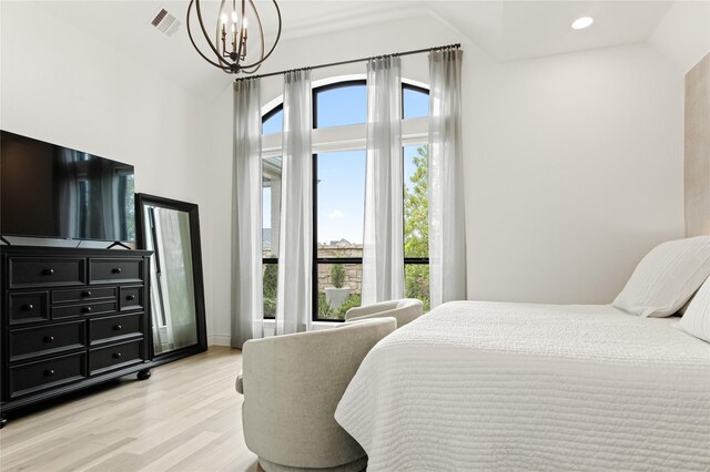 bedroom with a notable chandelier, lofted ceiling, and light wood-type flooring