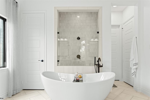 bathroom with plenty of natural light, tiled shower, baseboards, and a freestanding tub