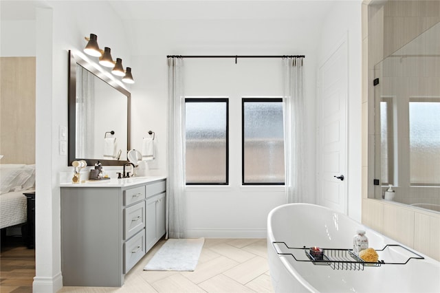 ensuite bathroom with ensuite bath, a freestanding bath, vanity, and baseboards