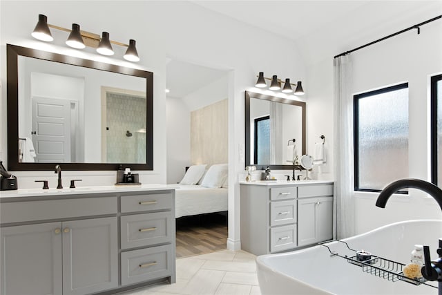 bathroom with a freestanding tub, two vanities, a tile shower, and a sink