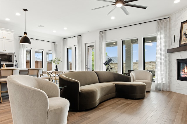 living room with ceiling fan, a fireplace, light hardwood / wood-style flooring, and plenty of natural light