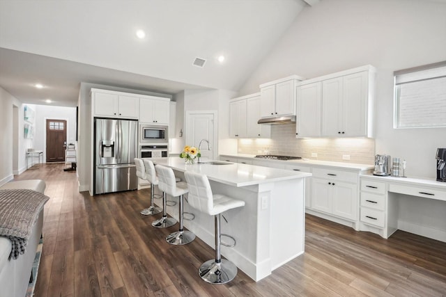 kitchen with high vaulted ceiling, an island with sink, sink, white cabinets, and stainless steel appliances