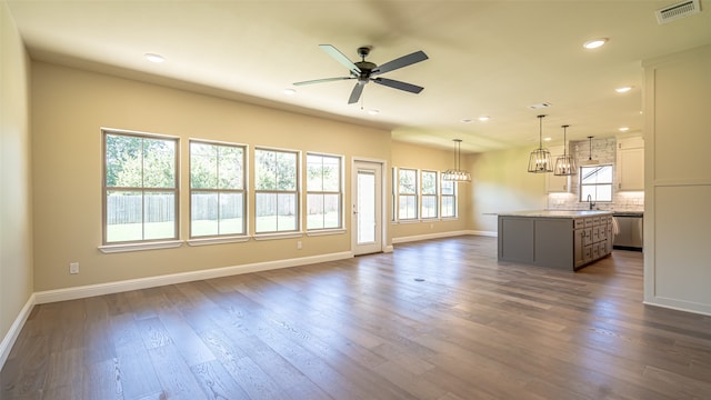 unfurnished living room featuring sink, ceiling fan with notable chandelier, and dark wood-type flooring