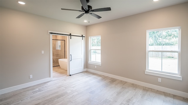 unfurnished bedroom with a barn door, ceiling fan, multiple windows, and connected bathroom