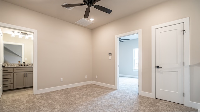 unfurnished bedroom featuring light colored carpet, ceiling fan, ensuite bathroom, and sink