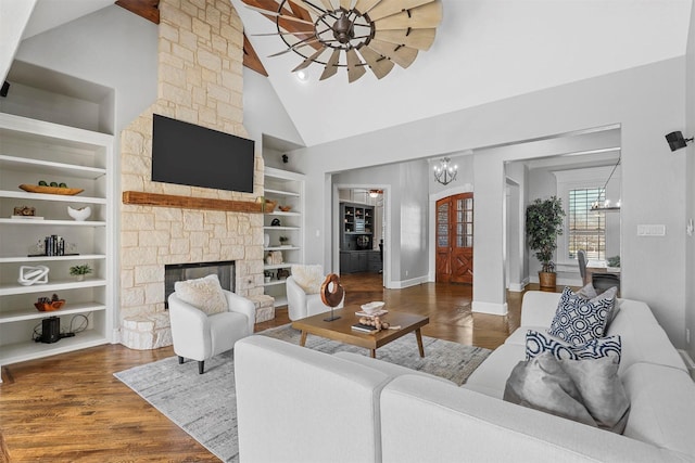 living room featuring a stone fireplace, an inviting chandelier, high vaulted ceiling, dark hardwood / wood-style flooring, and built in shelves