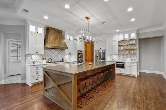 kitchen featuring an island with sink, appliances with stainless steel finishes, custom range hood, and white cabinets