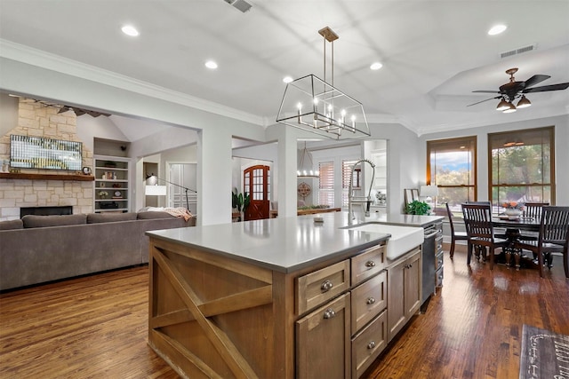 kitchen featuring ceiling fan with notable chandelier, built in features, a fireplace, sink, and a kitchen island with sink