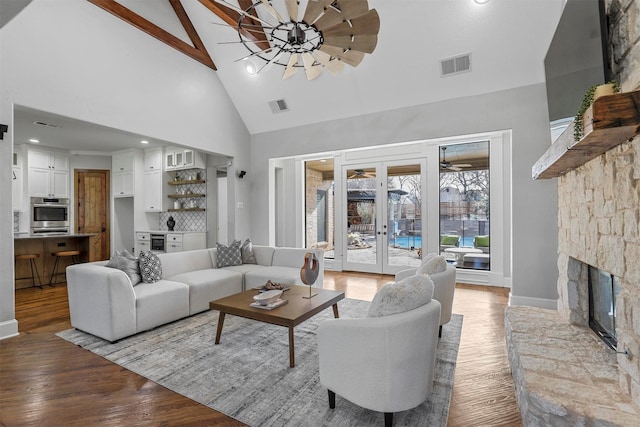 living room featuring french doors, a stone fireplace, wood-type flooring, high vaulted ceiling, and beamed ceiling