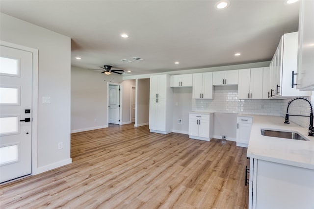 kitchen with white cabinetry, light stone counters, light wood-type flooring, ceiling fan, and sink