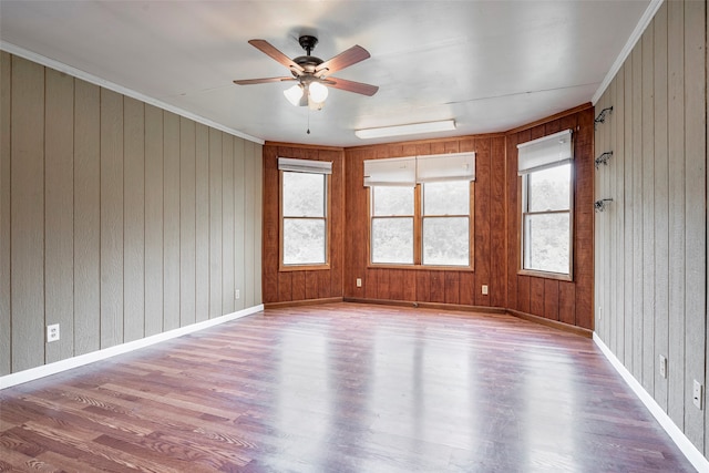 empty room with ceiling fan, crown molding, wood-type flooring, and wood walls