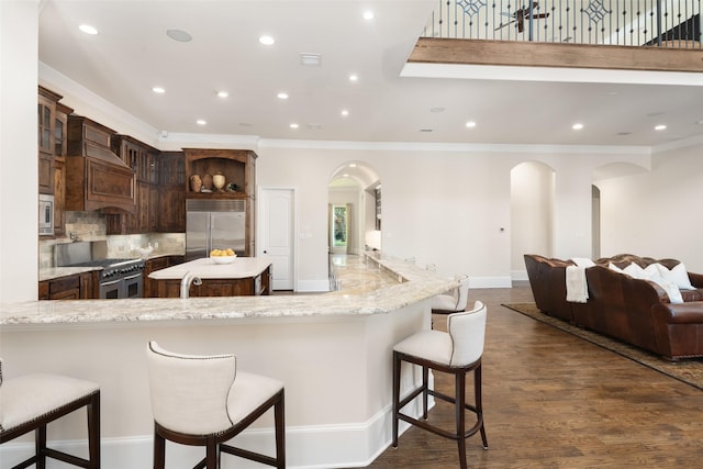 kitchen with glass insert cabinets, a peninsula, a kitchen bar, and built in appliances