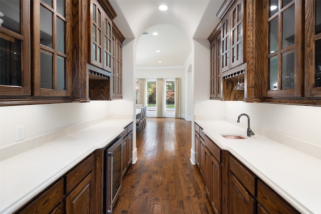 kitchen featuring dark brown cabinetry, wine cooler, ornamental molding, sink, and dark hardwood / wood-style flooring