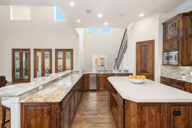 kitchen with french doors, a spacious island, stainless steel microwave, and a breakfast bar