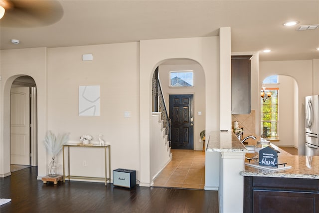 kitchen featuring dark brown cabinetry, light stone countertops, ceiling fan with notable chandelier, stainless steel fridge, and dark hardwood / wood-style flooring