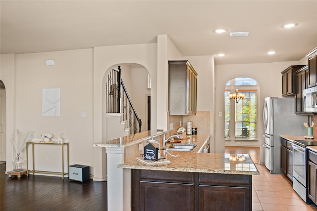 kitchen with light wood-type flooring, appliances with stainless steel finishes, light stone countertops, sink, and kitchen peninsula