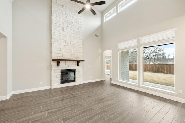 unfurnished living room featuring ceiling fan, a healthy amount of sunlight, a stone fireplace, and a high ceiling