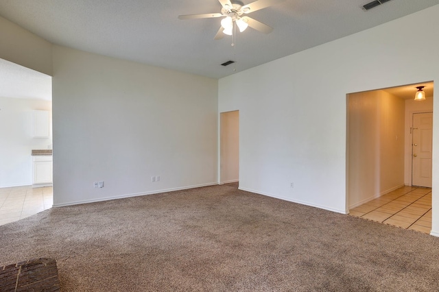 empty room featuring light carpet, light tile patterned floors, visible vents, and a ceiling fan