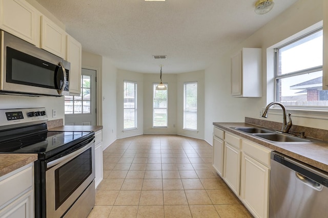 kitchen featuring white cabinets, dark countertops, appliances with stainless steel finishes, pendant lighting, and a sink