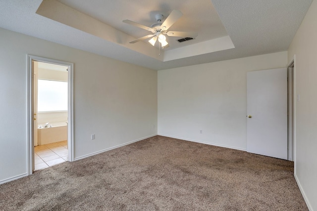 spare room featuring light tile patterned floors, a raised ceiling, light colored carpet, visible vents, and a ceiling fan