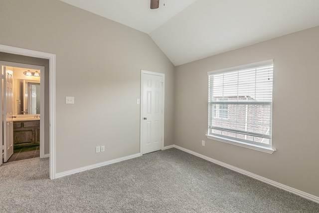 unfurnished bedroom featuring ensuite bath, ceiling fan, lofted ceiling, and carpet flooring