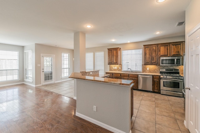 kitchen with sink, stainless steel appliances, a center island, light stone counters, and decorative backsplash