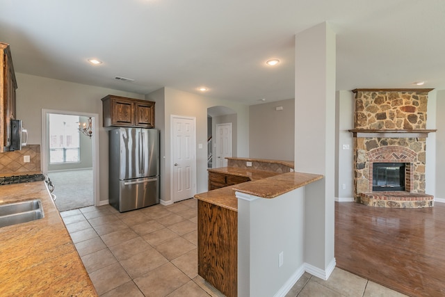 kitchen with stainless steel appliances, light stone countertops, light colored carpet, a stone fireplace, and backsplash