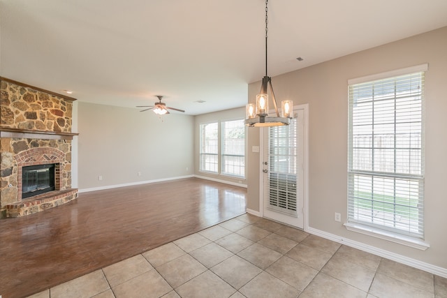 unfurnished living room with a stone fireplace, light hardwood / wood-style floors, and ceiling fan with notable chandelier