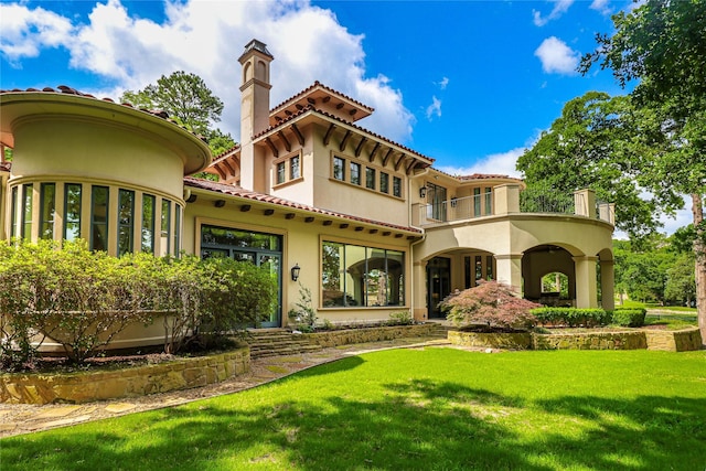 rear view of property featuring a tile roof, stucco siding, a chimney, a yard, and a balcony