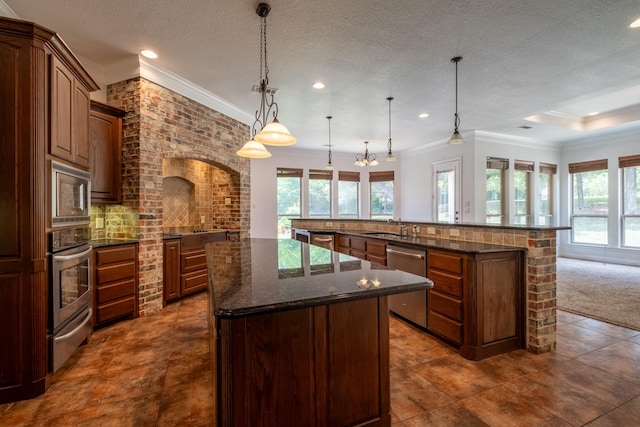 kitchen featuring a textured ceiling, appliances with stainless steel finishes, hanging light fixtures, a large island, and kitchen peninsula