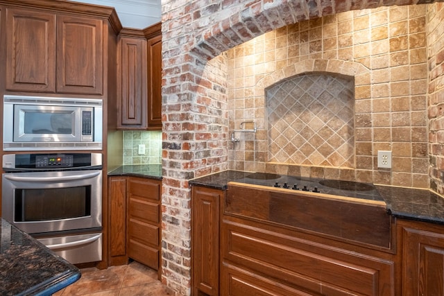 kitchen with backsplash, stainless steel appliances, dark stone counters, and light tile patterned flooring