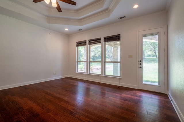 empty room featuring dark hardwood / wood-style flooring, ornamental molding, a raised ceiling, and a healthy amount of sunlight