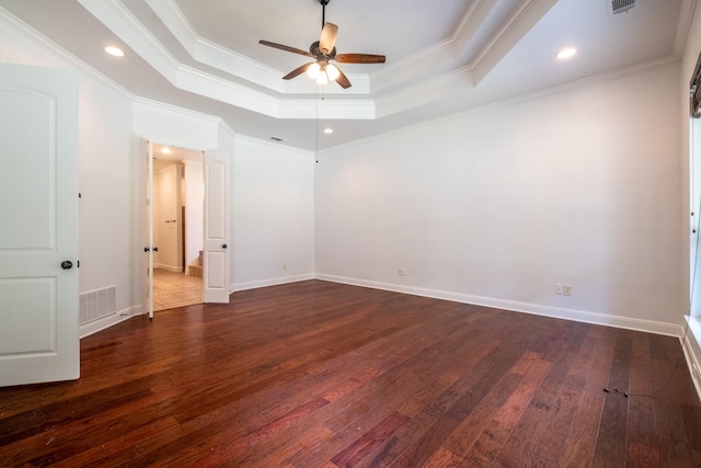 empty room featuring dark wood-type flooring, a tray ceiling, and crown molding